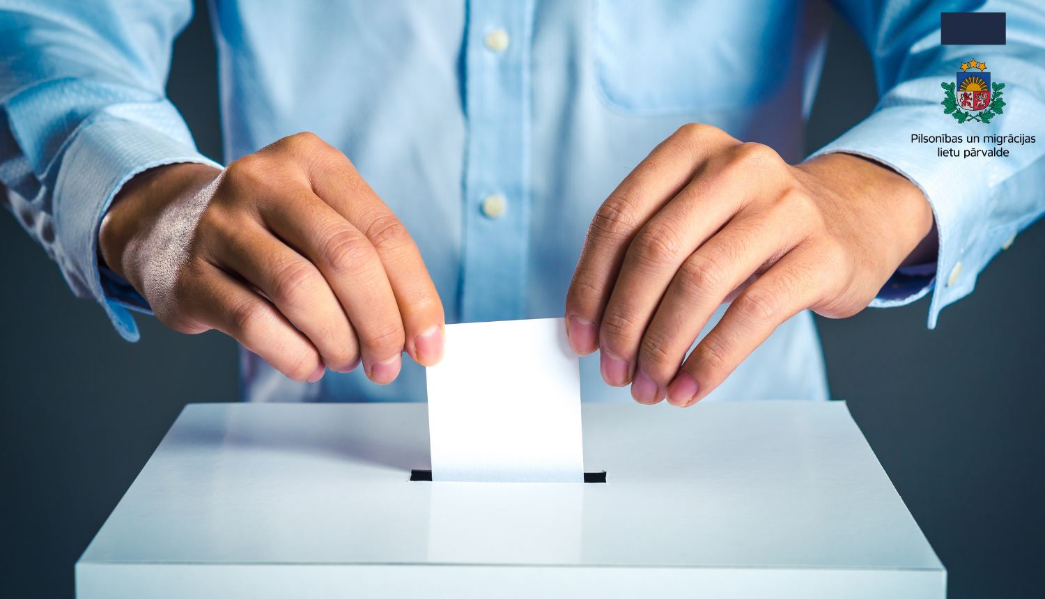 Cilvēka gaiši zilajā kreklā rokas, kas met aploksni vēlēšanu urnā 