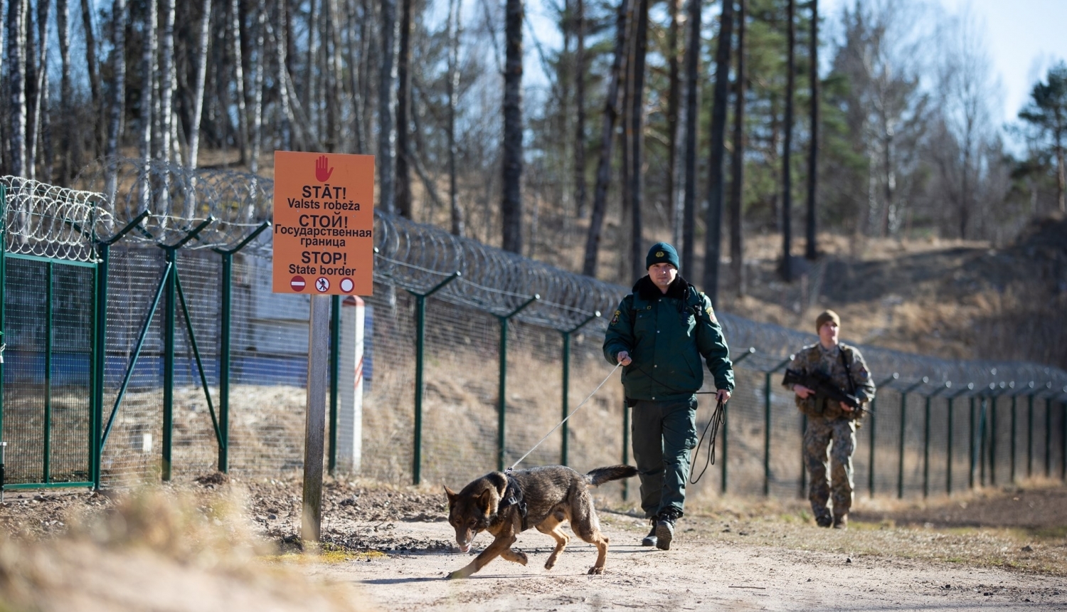 Divi robežsargi skrien gar robežu, viens ar suni, otram rokās - šaujamais ierocis